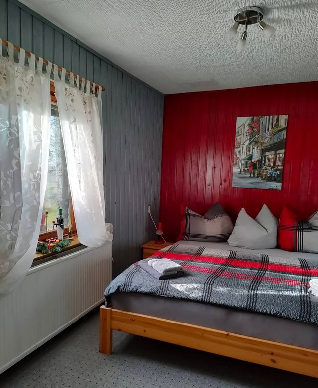 Schlafzimmer der Ferienwohnung mit roter Wand und Holzbett