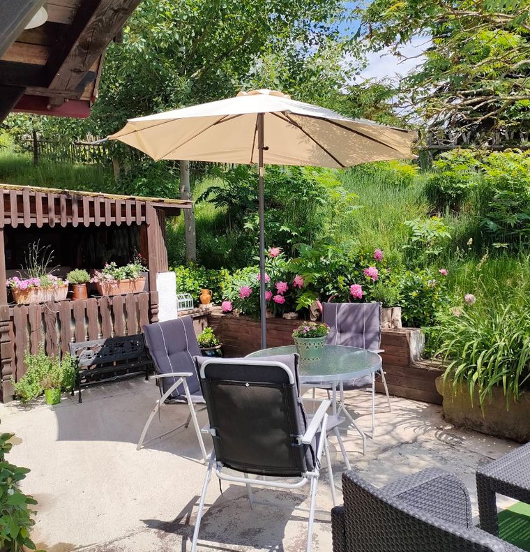 Sonnige Terrasse mit Sonnenschirm, Tisch und Blumen im Sommer